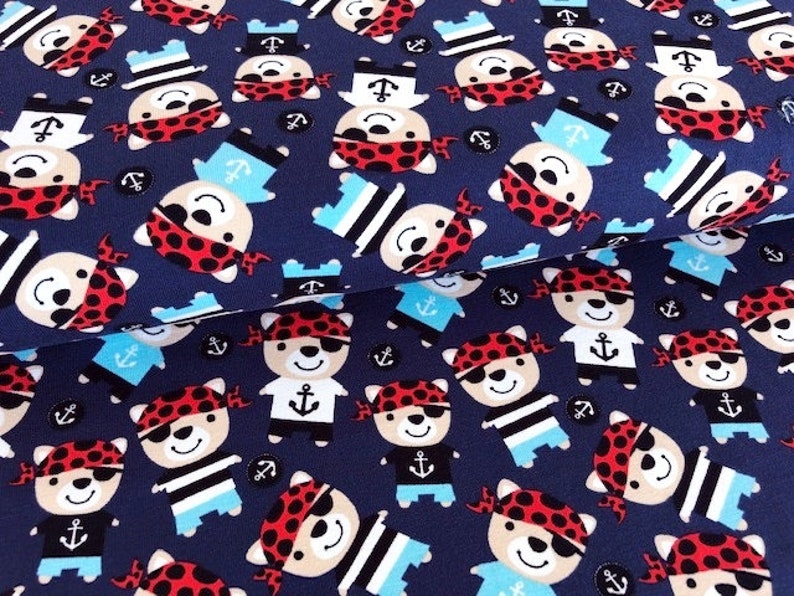 May include: Navy blue fabric with a repeating pattern of cartoon bear pirates wearing red bandanas, eye patches, and sailor hats. The bears have anchor designs on their shirts and are interspersed with anchor icons.