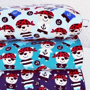 May include: Three rolls of fabric with a repeating pattern of cartoon pirate bears, anchors, and sailor shirts. The fabric colors are light blue, teal, and navy blue. The pirate bears wear red bandanas and eye patches.