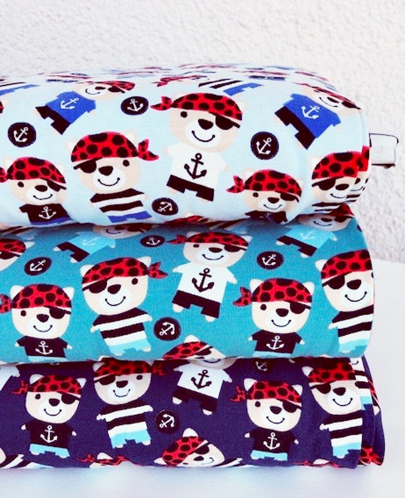 May include: Three rolls of fabric with a repeating pattern of cartoon pirate bears, anchors, and sailor shirts. The fabric colors are light blue, teal, and navy blue. The pirate bears wear red bandanas and eye patches.