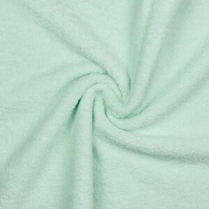 Könnte beinhalten: Nahaufnahme eines weichen, hellgrünen Handtuchs mit strukturierter Oberfläche. Das Handtuch ist gefaltet und verdreht, wodurch ein wirbelndes Muster entsteht.