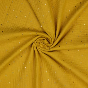 Könnte beinhalten: Senfgelber Stoff mit geknitterter Textur und verstreuten silbernen Metallic-Akzenten. Der Stoff ist in einer Spirale zusammengefasst, wodurch sein weicher Fall und subtiler Glanz hervorgehoben werden. Geeignet für Näh- und Bastelprojekte.