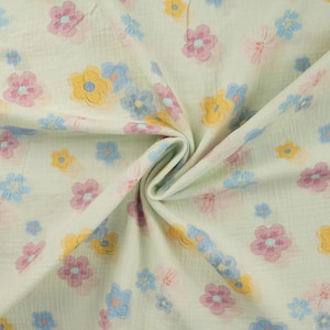 Könnte beinhalten: Cremefarbener Stoff mit einem sich wiederholenden Blumenmuster. Die Blumen sind in Rosa-, Gelb- und Blautönen gehalten. Der Stoff hat eine gekreppte Textur, was darauf hindeutet, dass es sich um Musselin oder ein ähnliches leichtes Material handelt. Ideal für Babydecken oder Sommerkleidung.