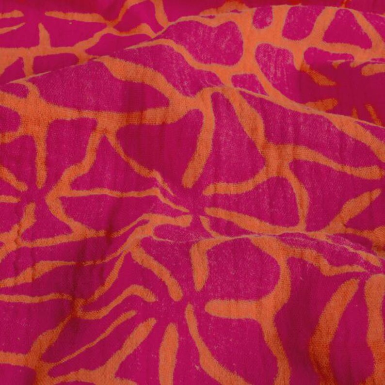 May include: Close-up of a fabric with a repeating floral pattern. The design features large, stylized flowers in a vibrant fuchsia pink color, outlined and filled with a warm orange hue. The fabric appears soft and slightly textured.
