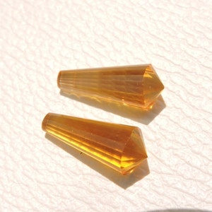 May include: Two amber-colored faceted glass teardrop-shaped beads. The beads are approximately 1 inch long and have a pointed tip.