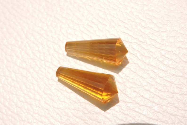 May include: Two amber-colored faceted glass teardrop-shaped beads. The beads are approximately 1 inch long and have a pointed tip.
