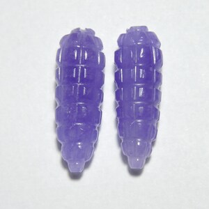 May include: Two purple carved jade beads, each shaped like a small, elongated cone with a textured surface.