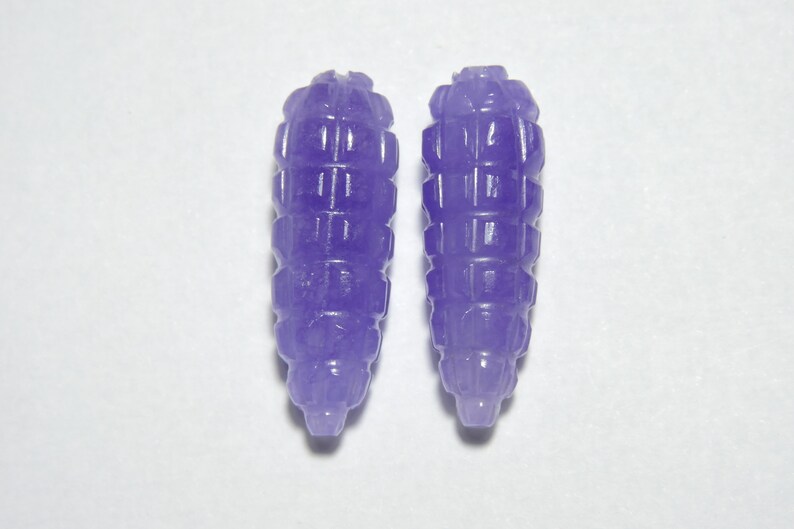 May include: Two purple carved jade beads, each shaped like a small, elongated cone with a textured surface.