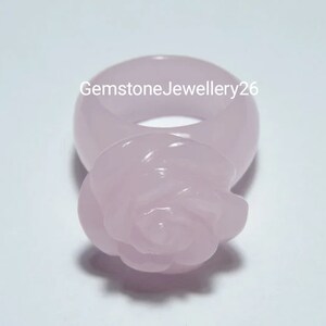 May include: A pale pink rose ring made of carved gemstone. The ring is a simple band with a rose carved on the top.