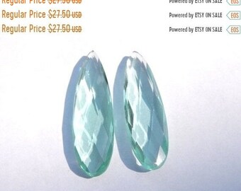 May include: Two teardrop-shaped, faceted, light blue glass beads. The beads are clear and have a slight green tint.