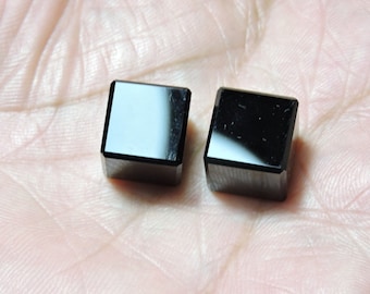 May include: Two black, cube-shaped gemstones with a polished, reflective surface.