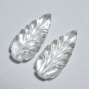 May include: Two clear quartz crystal leaves with intricate carved details. The leaves are smooth and polished.
