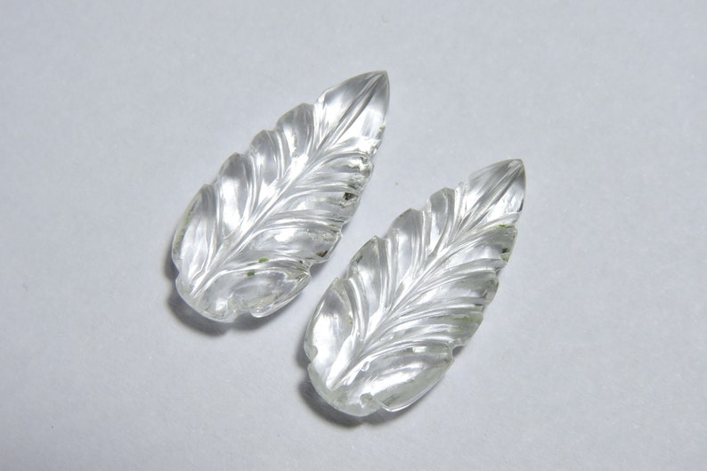 May include: Two clear quartz crystal leaves with intricate carved details. The leaves are smooth and polished.
