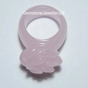 May include: A pale pink rose ring made of gemstone. The ring is carved in the shape of a rose with a smooth, polished finish.