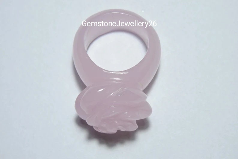 May include: A pale pink rose ring made of gemstone. The ring is carved in the shape of a rose with a smooth, polished finish.