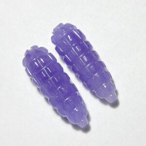 May include: Two purple carved gemstone beads with a textured design. The beads are approximately 1 inch long.
