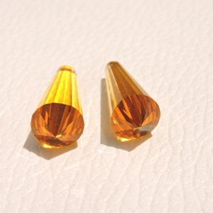 May include: Two amber-colored glass teardrop-shaped beads with a faceted design.