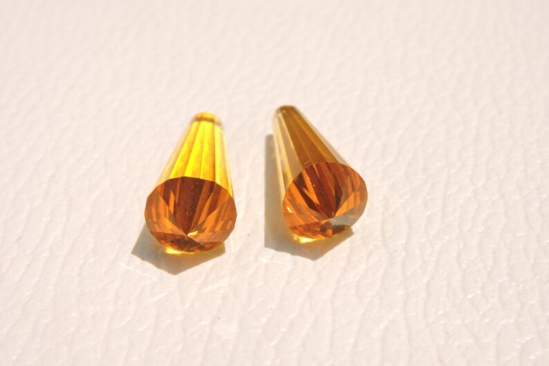 May include: Two amber-colored glass teardrop-shaped beads with a faceted design.