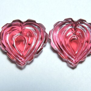 May include: Two pink heart-shaped glass beads with a faceted design.