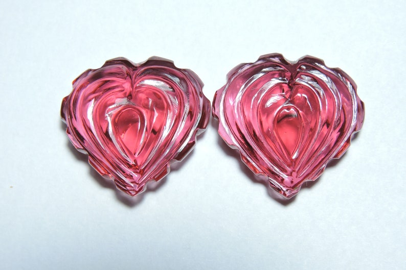 May include: Two pink heart-shaped glass beads with a faceted design.