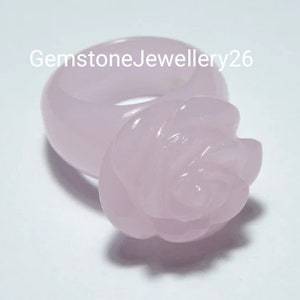 May include: A pale pink rose ring made of rose quartz. The ring is a simple band with a rose carved on top.
