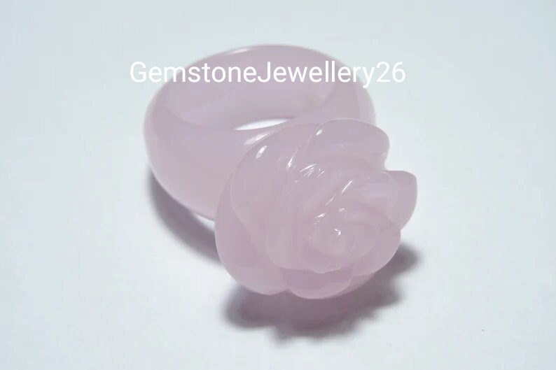 May include: A pale pink rose ring made of rose quartz. The ring is a simple band with a rose carved on top.