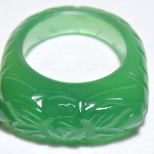 Puede incluir: Un anillo de jade verde con un diseño floral tallado. El anillo es liso y pulido.