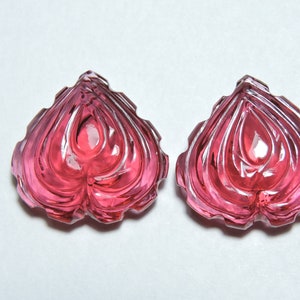 May include: Two pink heart-shaped carved gemstones with a faceted design.
