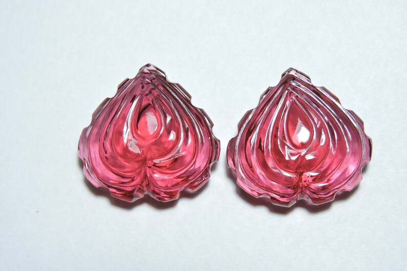 May include: Two pink heart-shaped carved gemstones with a faceted design.