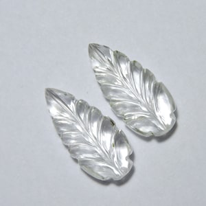 May include: Two clear quartz leaf-shaped carvings. The leaves are carved with detailed veins and have a smooth, polished finish.