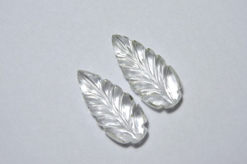 May include: Two clear quartz leaf-shaped carvings. The leaves are carved with detailed veins and have a smooth, polished finish.