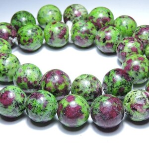 May include: A strand of green and pink gemstone beads. The beads are round and have a speckled pattern.