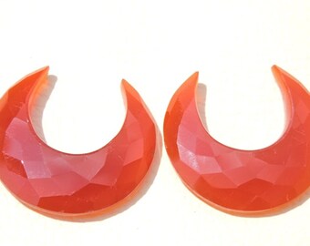 May include: Two crescent-shaped, faceted carnelian gemstone earrings in a bright orange color.