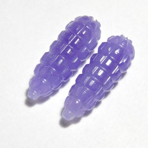May include: Two purple carved jade beads with a geometric design. The beads are smooth and polished.