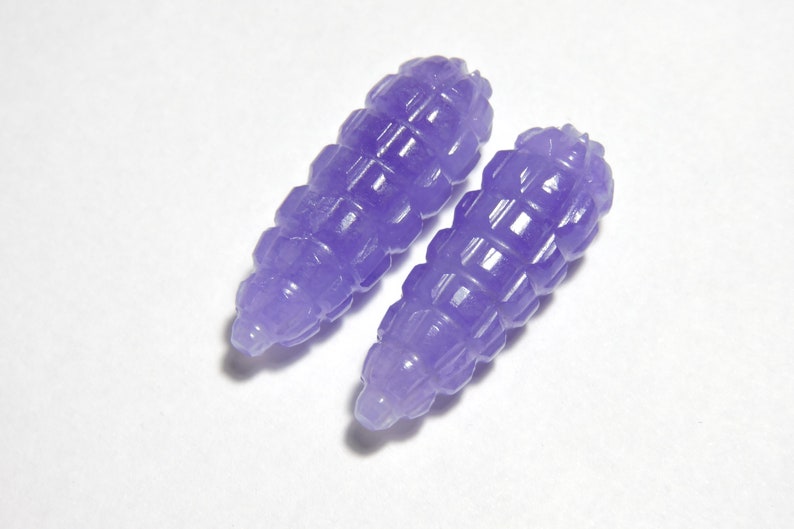 May include: Two purple carved jade beads with a geometric design. The beads are smooth and polished.