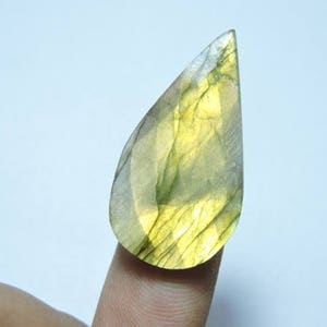 May include: A teardrop-shaped green and yellow labradorite gemstone with a smooth, polished surface.