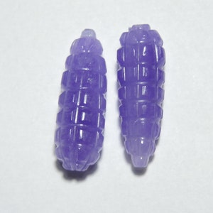 May include: Two purple jade beads with a textured, carved design. The beads are shaped like small, elongated barrels.