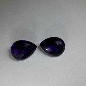 Pode incluir: Duas pedras preciosas de ametista facetadas em forma de l&aacute;grima, cada uma com um tom roxo profundo.