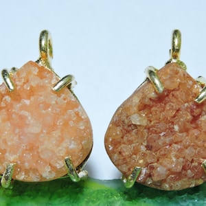 May include: Two teardrop-shaped pendants with gold-toned metal settings. The pendants are made of orange and brown crystal clusters.