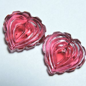 May include: Two pink heart-shaped glass pieces with a layered, textured design.