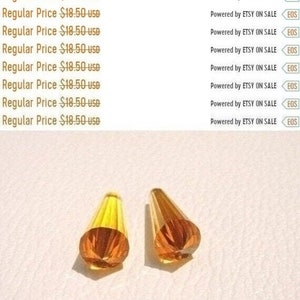 May include: Two amber glass teardrop-shaped crystal beads. The beads are faceted and have a shiny finish.