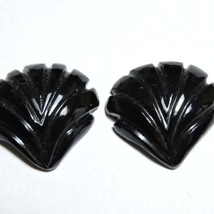 May include: Two black carved shell-shaped cabochons. The cabochons have a fan-like design with a pointed tip.