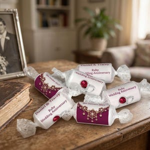 May include: Wrapped sweets with "Ruby Wedding Anniversary" text and a ruby ring graphic. A framed black and white wedding photo and a vintage book are on a wooden table. The sweets are white with burgundy accents.