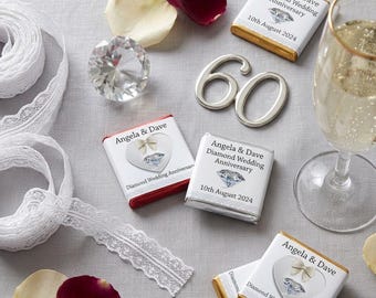 Może przedstawiać: Uroczysta aranżacja z czekoladkami, kieliszkiem szampana i diamentem. Czekoladki opatrzone są napisem "Angela & Dave Diamond Wedding Anniversary" z datą "10 sierpnia 2024". Biała koronkowa wstążka i liczba "60" również obecne.