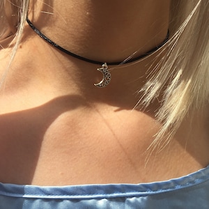 Puede incluir: Un collar gargantilla negro con un colgante de luna creciente plateado.