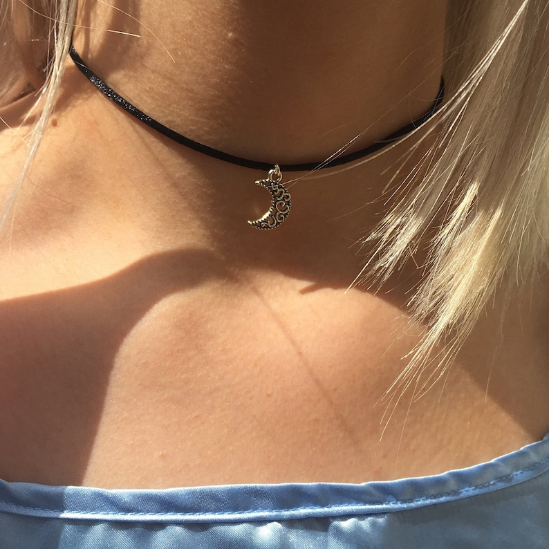 Puede incluir: Un collar gargantilla negro con un colgante de luna creciente plateado.