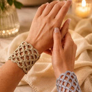 Peut inclure: Deux larges bracelets de poignet présentant un motif complexe en crochet ajouré. L'un est de couleur beige clair, tandis que l'autre est d'une teinte lavande douce. Les deux accessoires sont faits d'un cordon texturé en treillis.