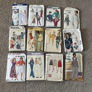 May include: A collection of twelve vintage sewing pattern envelopes from brands including Butterick, Simplicity, and McCall's. Each paper envelope features illustrations of various clothing styles such as dresses, blouses, skirts, and trousers, along with printed brand names and pattern numbers.