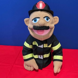 Puede incluir: Un títere de mano marrón que lleva un uniforme de bombero negro con rayas amarillas y un sombrero de bombero negro con un emblema rojo del departamento de bomberos. El títere tiene bigote y una boca rosa.