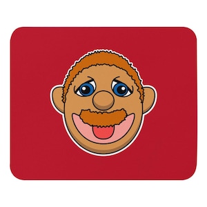 Puede incluir: Ilustración de un rostro de dibujos animados con piel morena, ojos azules, bigote rojo y lengua roja. El rostro está sobre un fondo rojo, en un cuadrado redondeado.