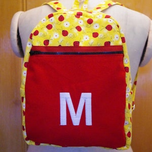 Op de afbeelding: Een rode en gele rugzak met lieveheersbeestjesprint, een ritsvak en een witte geborduurde letter "M" aan de voorkant.